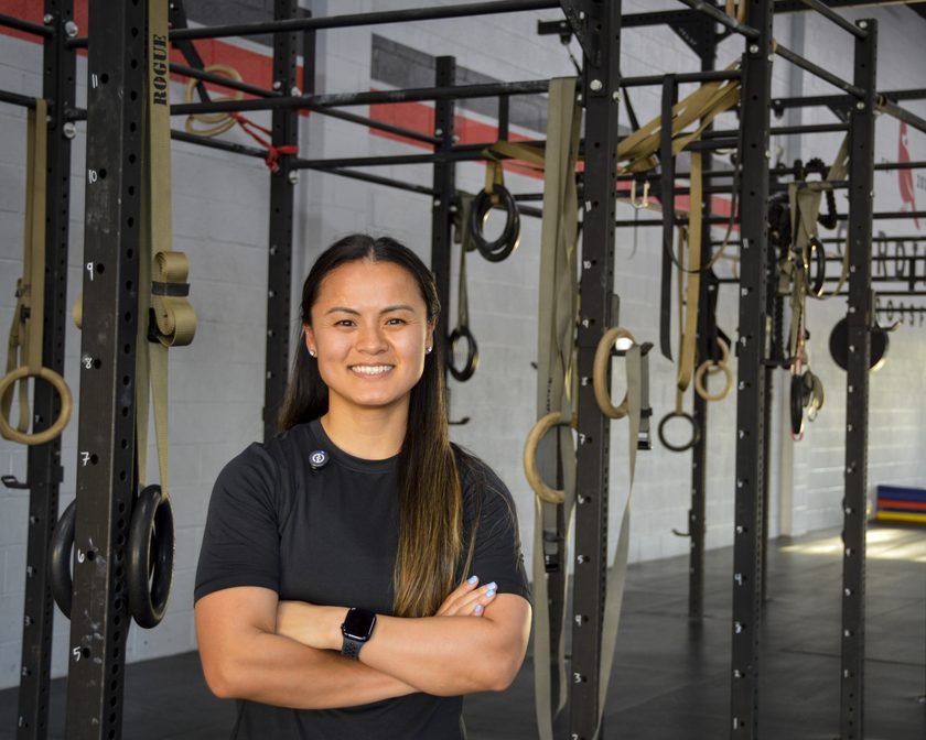 Dr. Amy Driessen, physical therapist, standing with her arms folded in front of a gymnastics rig and rings inside the gym where she treats patients.